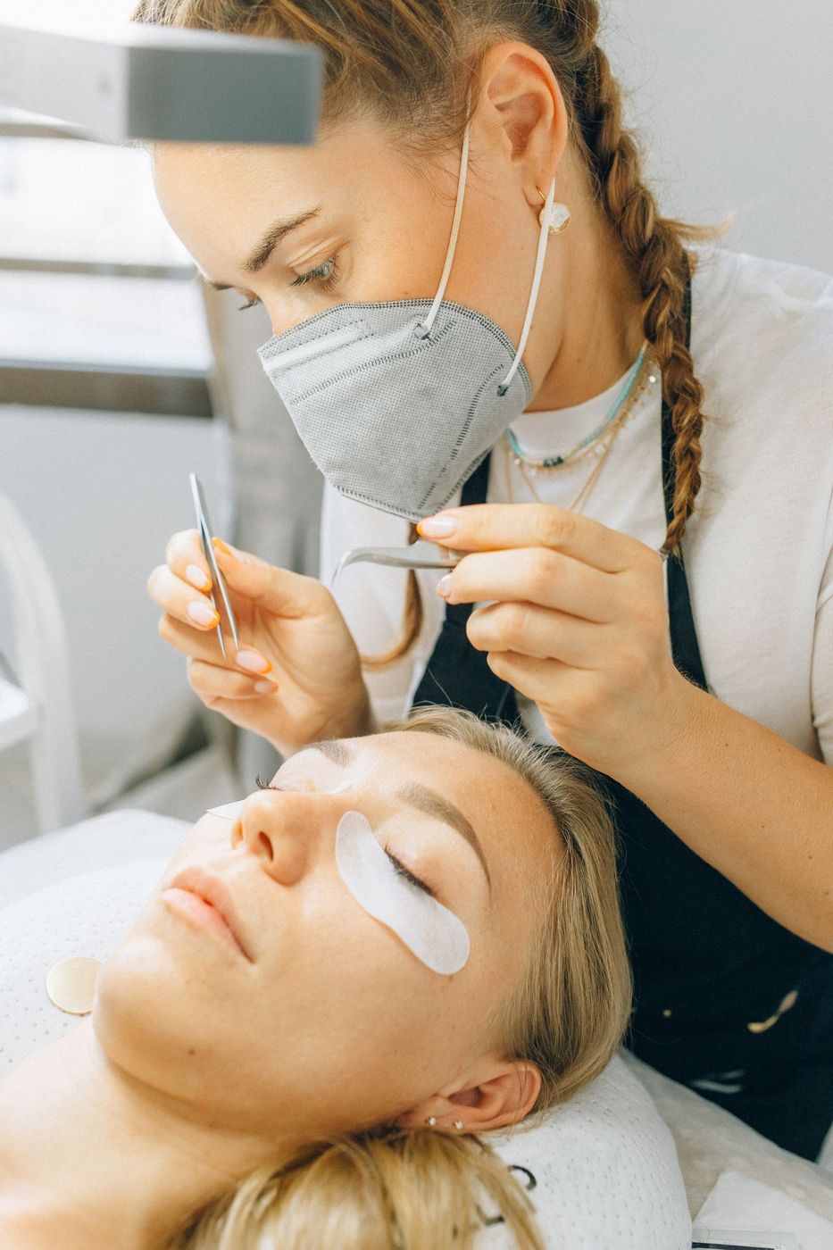 Lash designer aplicando extensão de cílios com pinça em uma cliente deitada